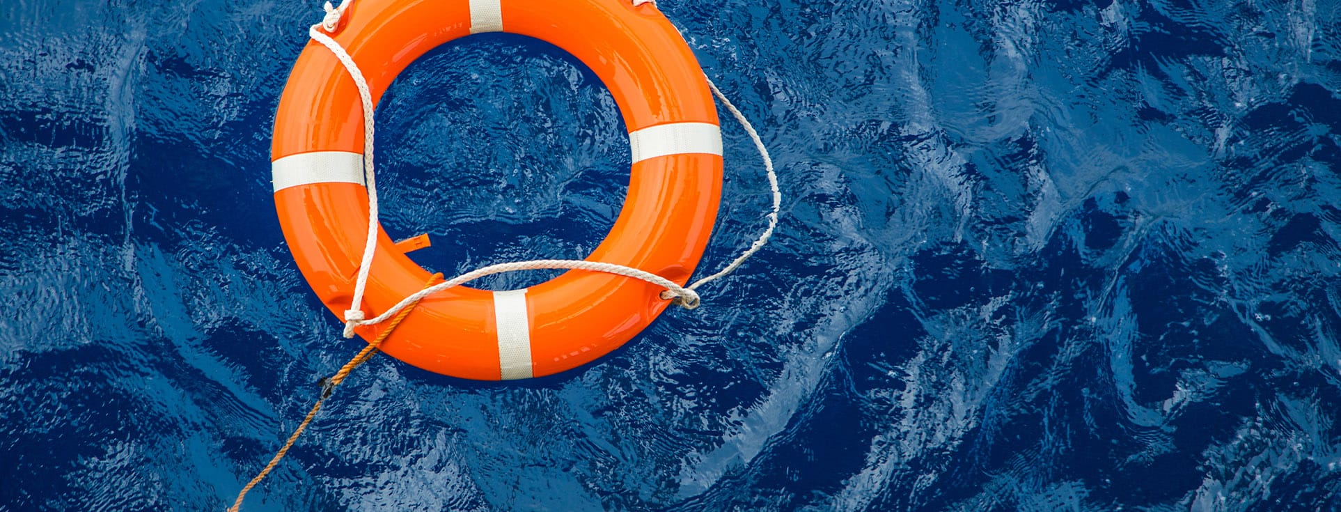 A bright orange life ring with white stripes floats on deep blue water, attached to a rope.